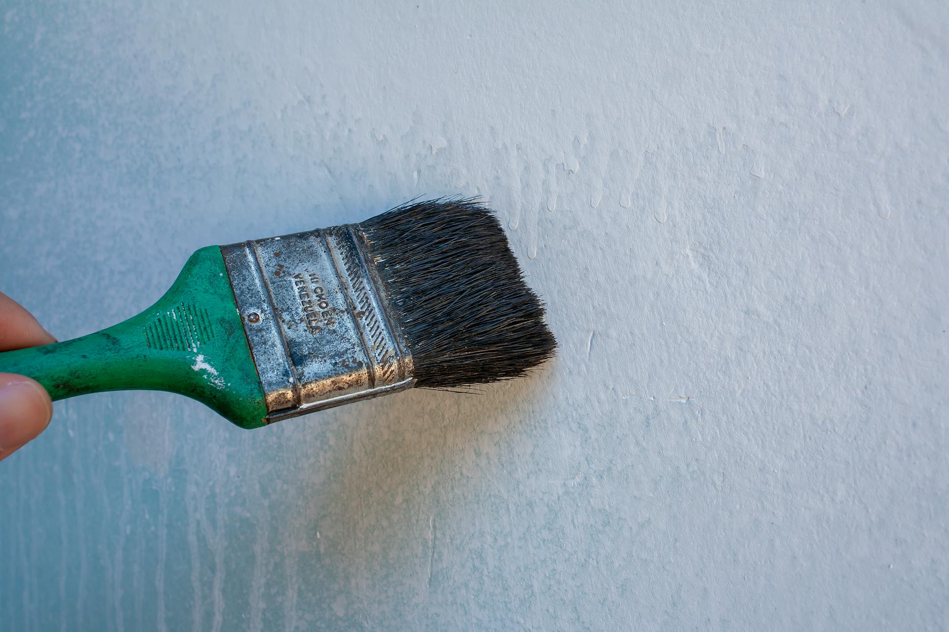 Close-up of a hand painting an interior wall with a brush.